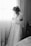 A person stands in front of a window with delicate sheer curtains, holding up a detailed bridal gown adorned with floral appliques. The individual has hair styled in rollers and is wearing a robe. The setting is a cozy room with soft lighting.