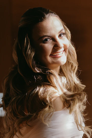 A warm, inviting photo of a confident woman smiling softly, surrounded by soft pink and gold tones.