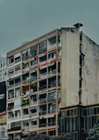 A multi-story building facade with numerous signs and logos indicating various businesses, eateries, and cafes. The building has a slightly worn appearance with some discoloration and aging on the walls, contributing to an urban, gritty atmosphere. The signs display a mix of diverse and colorful branding, suggesting a lively commercial area.