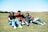 A group of friends laughing and playing games together on mobile devices outdoors.