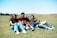 A group of friends laughing and playing games together on mobile devices outdoors.