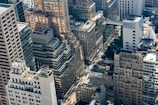 A dense urban landscape featuring a variety of high-rise buildings. The architecture includes a mix of modern and older styles, with glass facades and masonry. The streets below are bustling with traffic and people, and there is a visible network of streets and intersections.