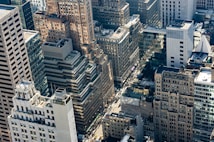 A dense urban landscape featuring a variety of high-rise buildings. The architecture includes a mix of modern and older styles, with glass facades and masonry. The streets below are bustling with traffic and people, and there is a visible network of streets and intersections.