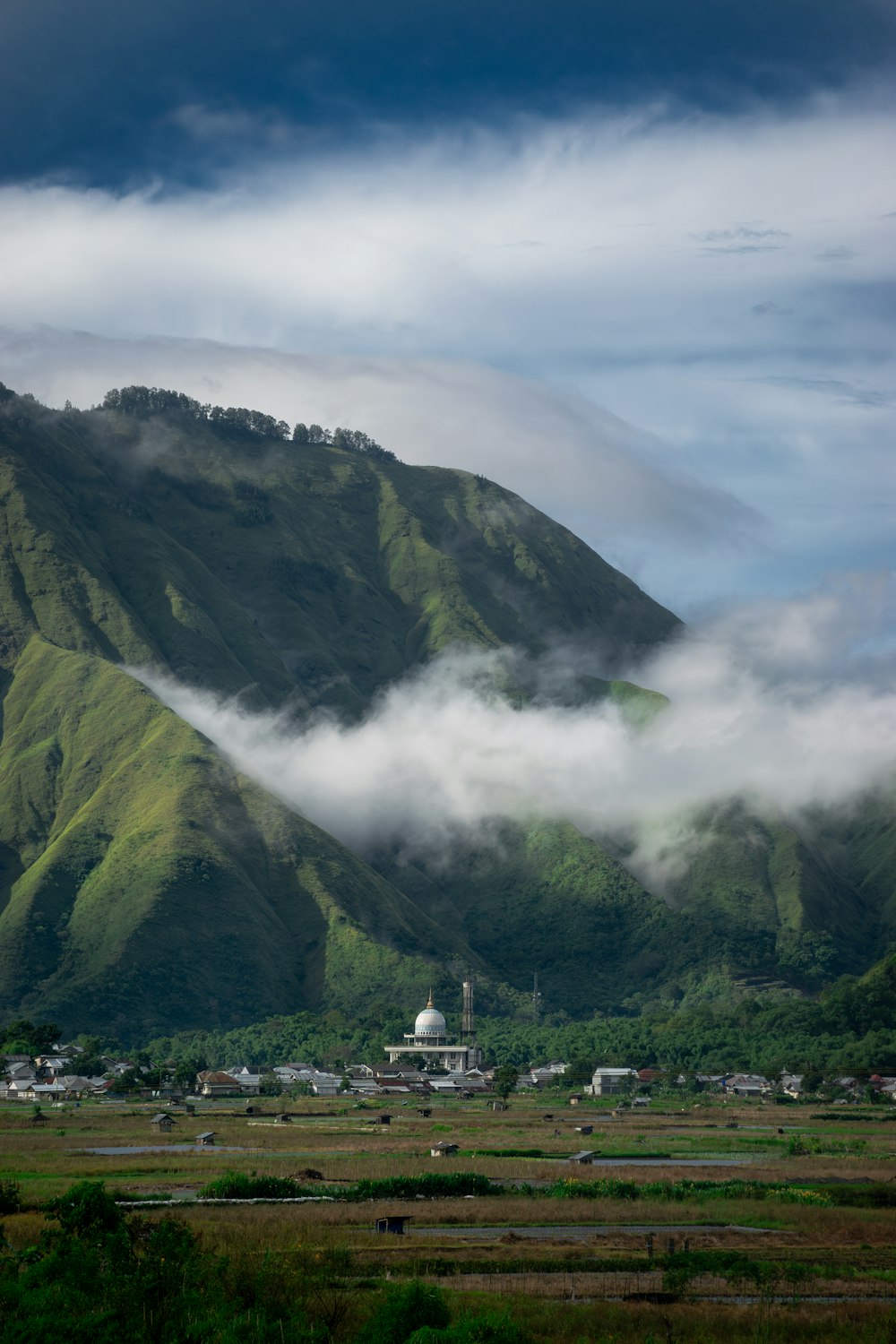 una montaña cubierta de nubes con un pueblo en primer plano