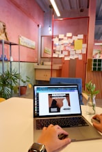 A friendly admin assisting a host with a laptop in a cozy, pastel-colored workspace.