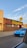 A vibrant blue sports car is parked in front of a brick building with a large sign that reads 'Ridgewood.' The sign is in bold, yellow lettering. There's a person standing near the building's entrance under the clear blue sky.