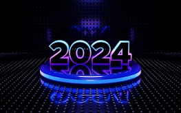 A futuristic setting featuring the glowing number 2024 prominently placed on a circular platform. The digits are illuminated with a blend of blue and purple hues. The background is a dark, perforated wall with a reflective floor that adds to the high-tech, digital aesthetic.