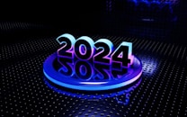 A bold and futuristic representation of the year 2024 is set against a dark, metallic background with circular patterns. The numbers are illuminated with a gradient of blue and purple lights, creating a reflective effect on the glossy surface below.
