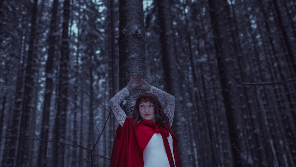 a woman in a red cape standing in a forest