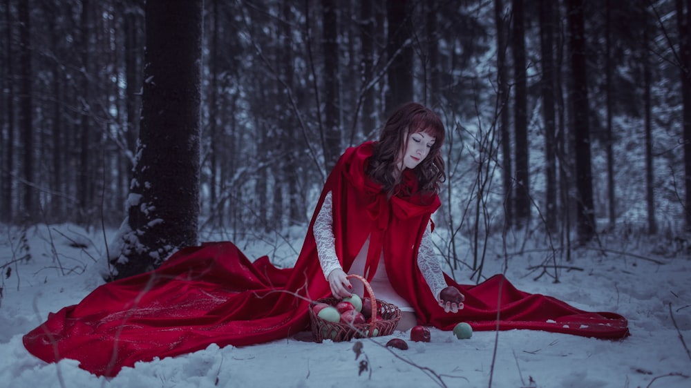 a woman in a red cloak sitting in the snow