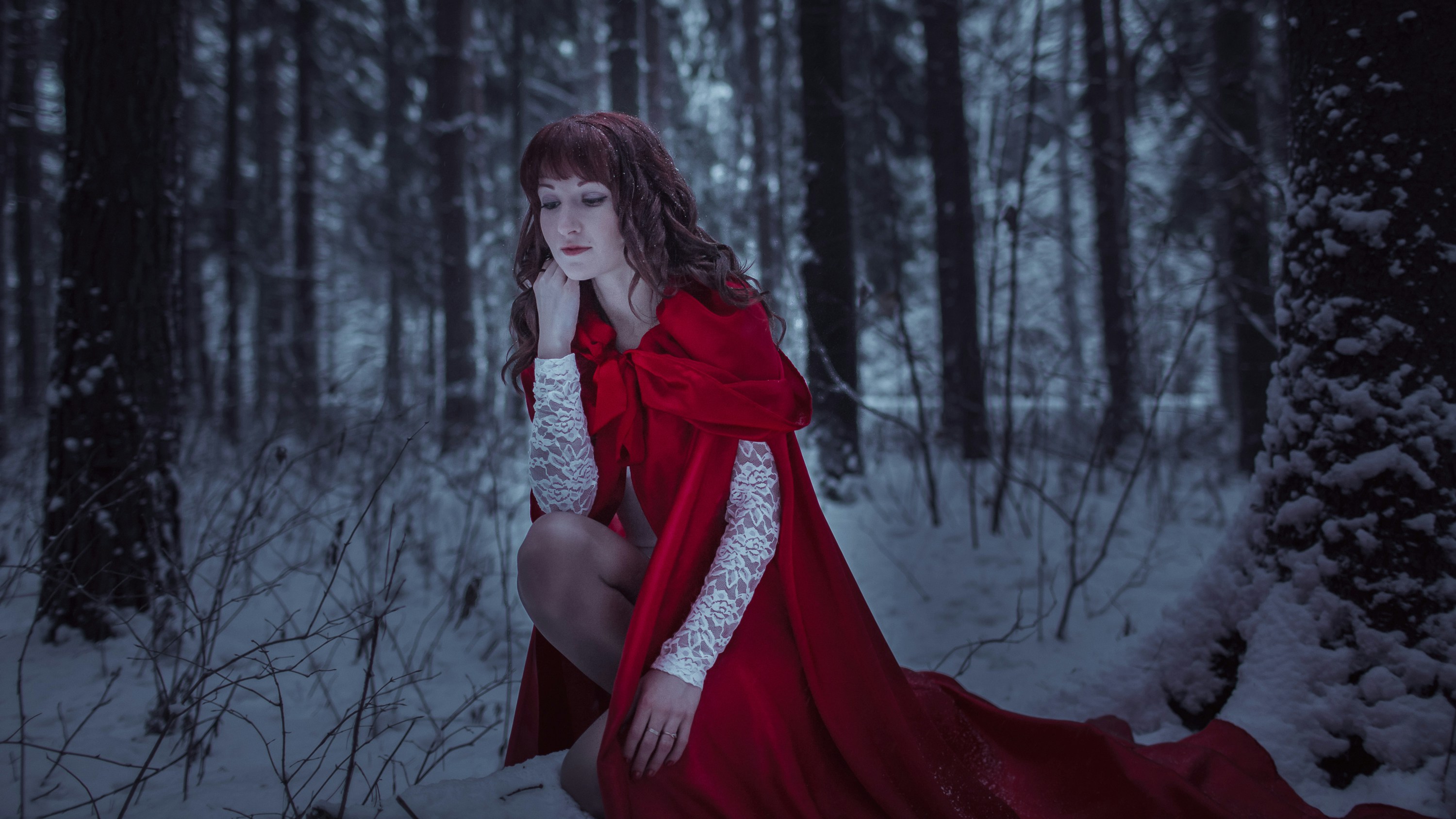 a woman in a red dress crouches in a snowy forest