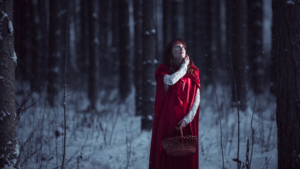 une femme en manteau rouge dans une forêt enneigée