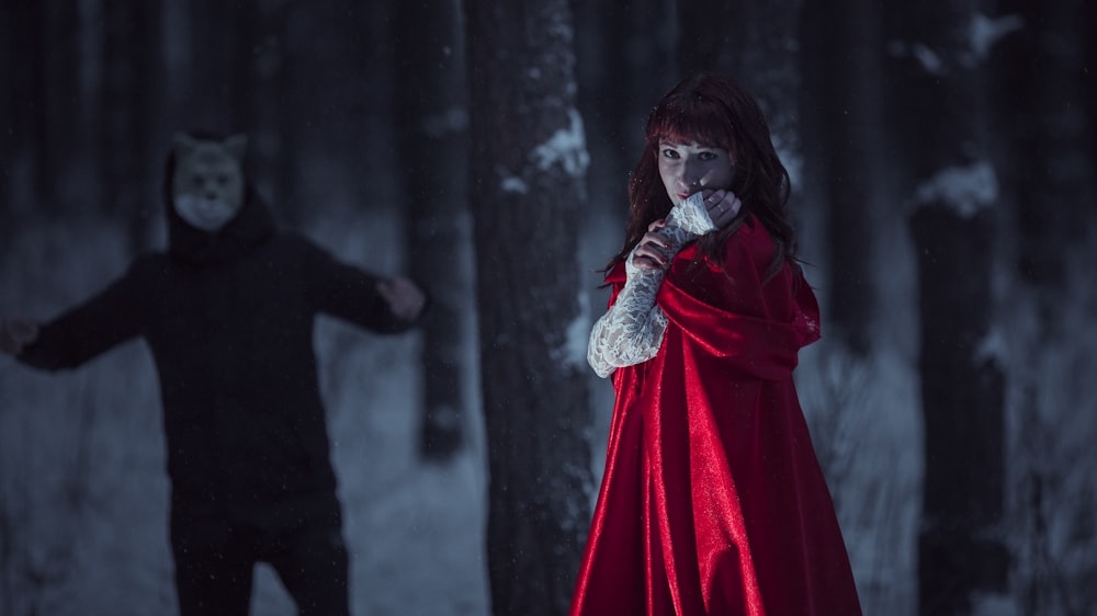 a woman in a red cloak standing next to a man in a black coat