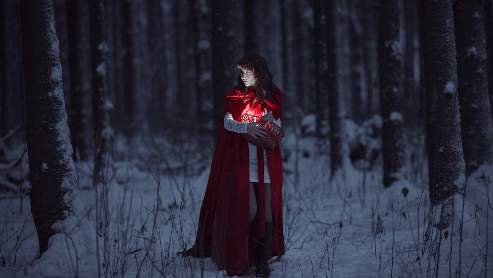 une femme dans une cape rouge tenant un cœur dans une forêt enneigée