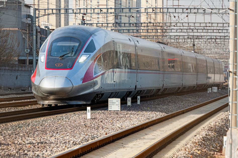 a silver train traveling down train tracks next to tall buildings