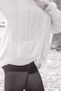 A person wearing a textured, knitted cardigan with cable patterns and buttons, paired with dark leggings. The focus is on the clothing details, including the pocket and the knit stitching.