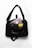 A black shoulder bag with a text design on the front. Inside, there are various electronic items including a laptop, a smartphone with a three-camera setup, a pair of wireless earbuds, and a yellow book with a patterned cover. The bag is placed on a white surface.