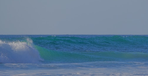 A serene ocean scene with gently rolling waves under a clear sky, displaying shades of blue and green with some foamy white caps on the waves.