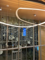 A modern indoor space featuring a high ceiling with wooden panels. Elegant, looped light fixtures hang from above, and illuminated decorative spheres are arranged artistically against a backdrop of large windows. Outside, city lights can be faintly seen through the glass.