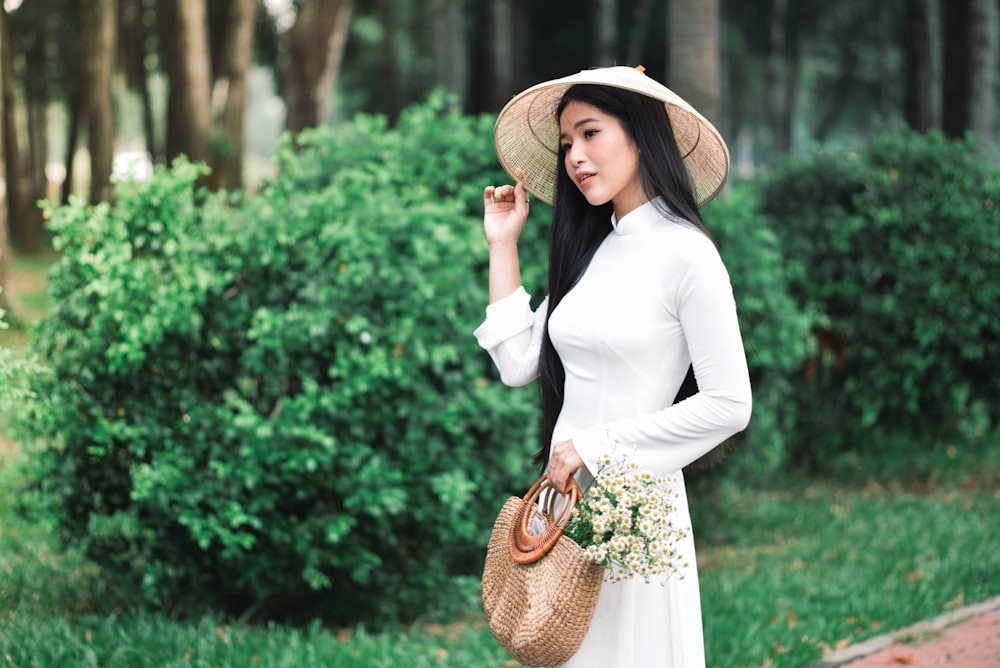 uma mulher em um vestido branco segurando um chapéu de palha