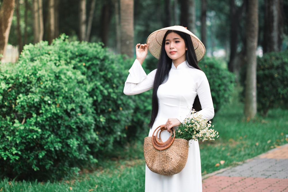 uma mulher em um vestido branco e chapéu segurando uma cesta