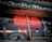A storefront window with a bright red neon sign advertising books, CDs, videos, and comics. Inside the window display, there are various items including musical instruments like a guitar and a drum, along with vintage records. The exterior is somewhat retro, with a rustic sign on top and reflections from the street.
