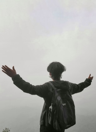 A serene figure standing atop a mountain at sunrise, arms wide open embracing freedom.