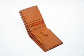 A brown leather wallet with a textured finish is open, revealing several compartments including a zipper pocket and slots for cards.
