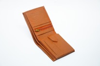 A brown leather wallet with a textured finish is open, revealing several compartments including a zipper pocket and slots for cards.