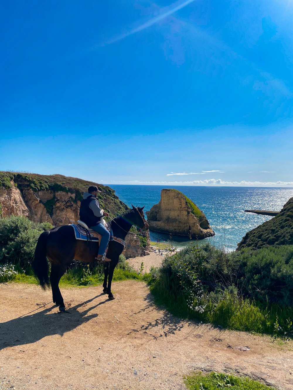 um homem montado em um cavalo em uma estrada de terra ao lado do oceano