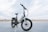 A sleek, modern electric bike stands on a paved surface with a vast, open background. The bike has a sturdy frame, large tires, and is equipped with a suspension fork. The brand name is visible on the frame, and the bike seems ready for both urban and off-road adventures.