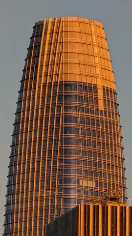 A sleek, modern office tower illuminated by a soft orange glow symbolizing a guiding beacon at dusk.