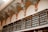 A high-ceilinged room with ornate decorative arches featuring intricate patterns and flourishes. Below the arches, there is a series of wooden shelves with ornately designed metal railings. The shelves are lined with books or files, organized in a neat and orderly manner.