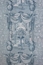 A detailed and intricate wallpaper pattern with symmetrical design elements. Two large urns feature decorative patterns and are flanked by stylized foliage. A central vase holds an ornate bouquet of flowers, framed by draped fabric and tassels. The background displays lattice patterns, and scenes reminiscent of classical art appear within the frames.