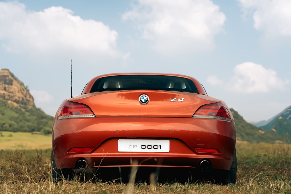 a red car parked in a field with mountains in the background