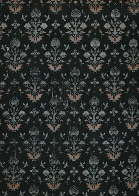 A dark, intricately patterned wallpaper featuring symmetrical floral designs. The repeating motifs include stylized flowers and leaves, along with subtle butterfly shapes, all rendered in muted shades of green, white, and orange.