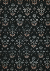 A dark, intricately patterned wallpaper featuring symmetrical floral designs. The repeating motifs include stylized flowers and leaves, along with subtle butterfly shapes, all rendered in muted shades of green, white, and orange.