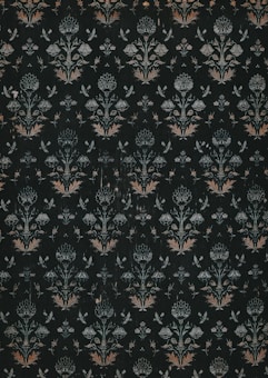 A dark, intricately patterned wallpaper featuring symmetrical floral designs. The repeating motifs include stylized flowers and leaves, along with subtle butterfly shapes, all rendered in muted shades of green, white, and orange.