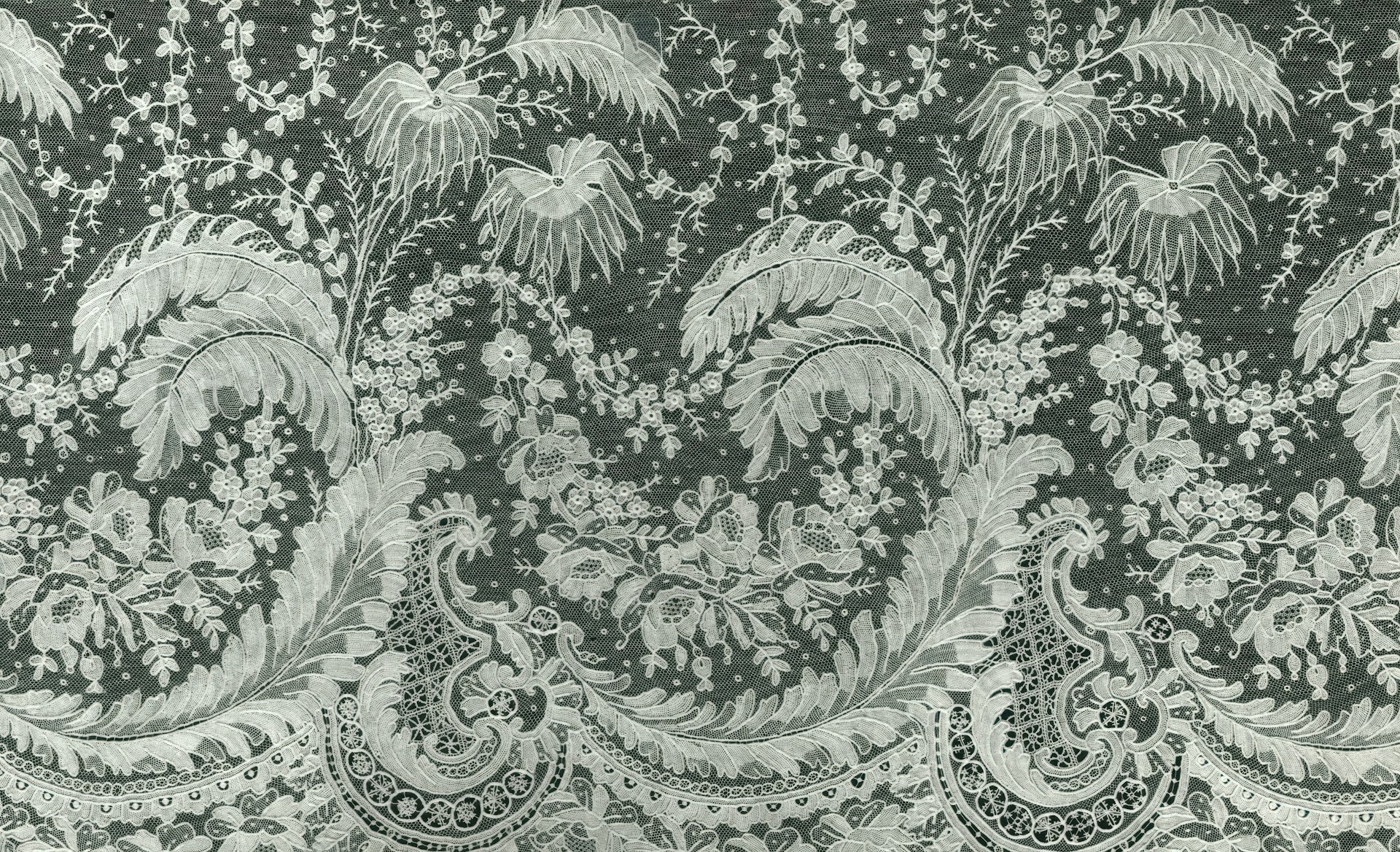 Close-up of delicate floral alpana motifs woven subtly into the off-white cotton fabric of a banglar tant saree, highlighted by warm golden accents.