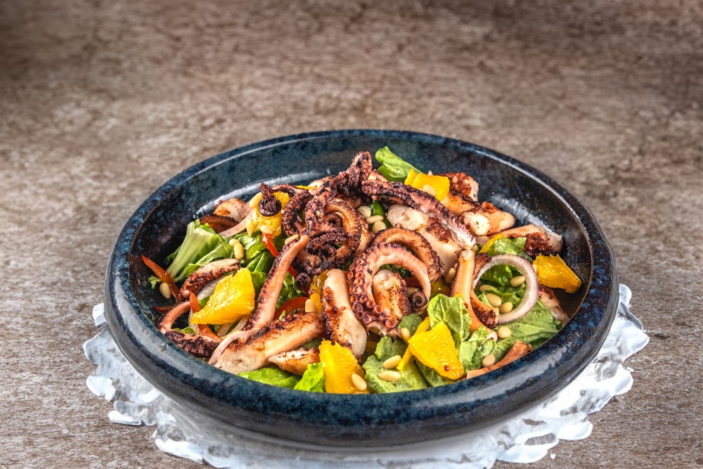 a blue bowl filled with a salad covered in octopus