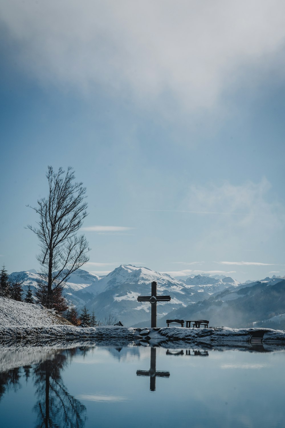 a cross is reflected in the still water of a lake