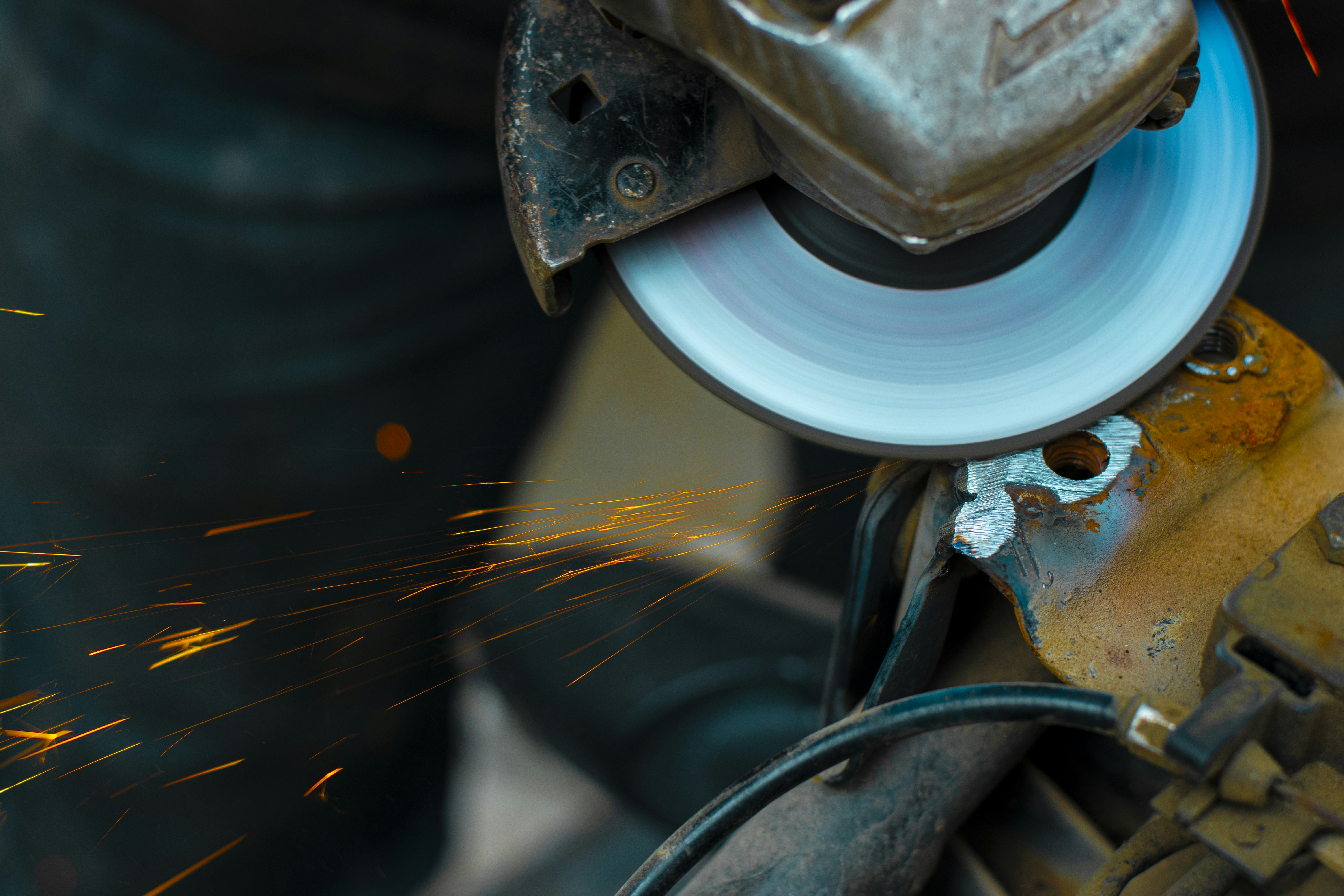 Angle grinder with sparks flying during metal grinding in dark industrial workshop, dramatic spark shower, atmospheric low-key lighting