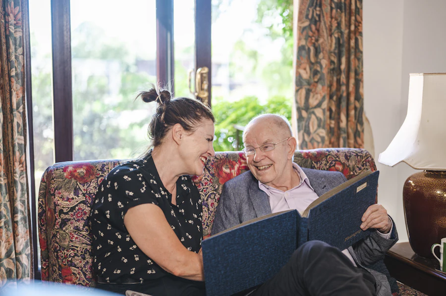 A caregiver and a senior man sitting together on a couch, talking