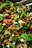 A close-up of a colorful salad with lentils, diced cucumbers, chopped red bell peppers, sliced red onions, fresh mint leaves, and assorted leafy greens. The ingredients appear freshly chopped and mixed together, with a shiny, vibrant appearance suggesting freshness and flavor.