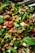 A close-up of a colorful salad with lentils, diced cucumbers, chopped red bell peppers, sliced red onions, fresh mint leaves, and assorted leafy greens. The ingredients appear freshly chopped and mixed together, with a shiny, vibrant appearance suggesting freshness and flavor.
