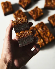Close-up of a hand holding a rich piece of carob chocolate against a backdrop of Beni Mellal’s natural landscape.