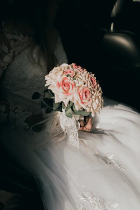 Softly lit image of a bride's hand clutching a colorful floral bouquet blending warm tones.