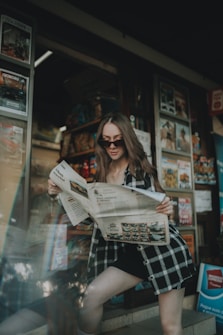 a woman is reading a newspaper outside of a store