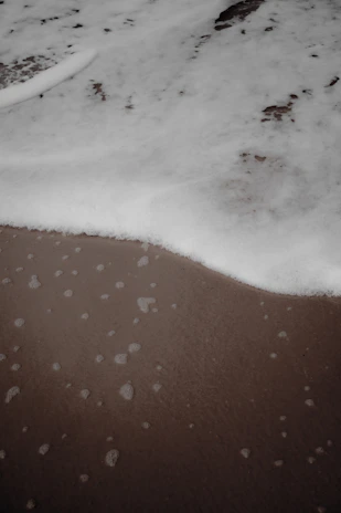 Close-up of sea foam delicately washing over dark sand under soft natural light.