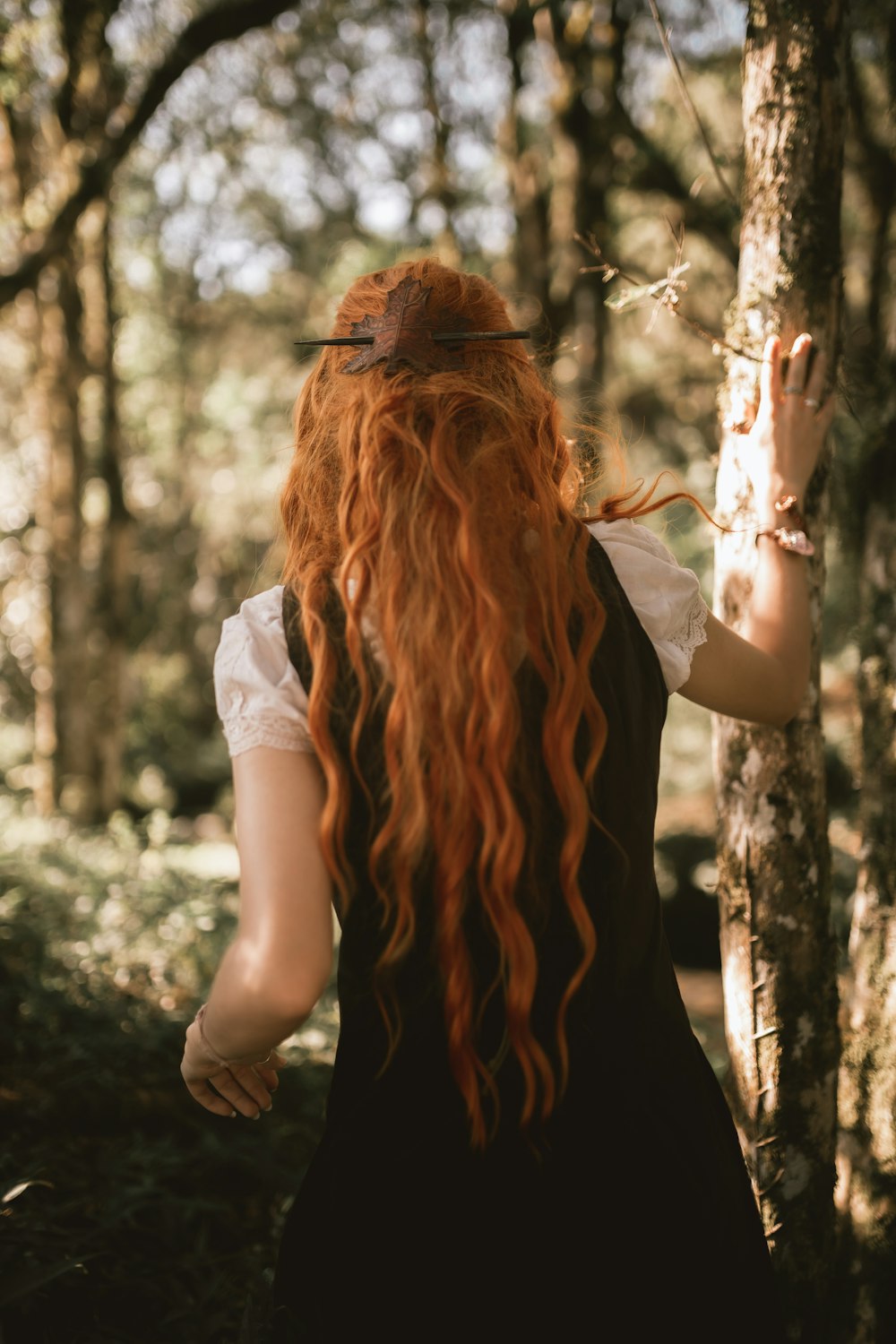 a woman with long red hair walking through a forest